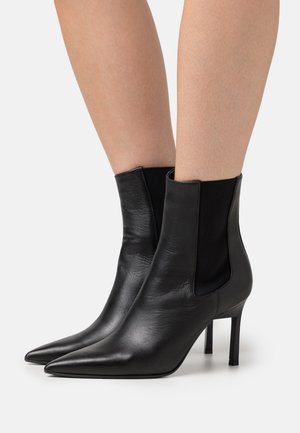 Bottines en cuir noir avec des bouts pointus, des panneaux latéraux élastiques et des talons aiguilles fins. La texture semble lisse et brillante.
