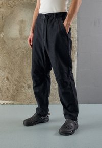 Czarne, luźne spodnie z paskiem, z bocznymi kieszeniami i szwami na kolanach. W połączeniu z czarnymi, gumowymi klapkami. Gładka tekstura i swobodny styl.