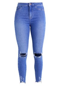 Jeans ajustados en denim azul medio con cintura alta, desgastes en las rodillas y dobladillo desflecado. Textura suave y diseño entallado.
