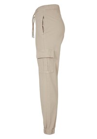 Pantalon jogger cargo beige avec taille élastique, lien coulissant, poches latérales, poche à rabat sur la cuisse et poignets élastiques aux chevilles.