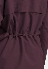 Burgunderfarbene Oberbekleidung mit geraffter Taille, weicher Textur und schichtiger Gestaltung. Der Stoff ist glatt mit mattem Finish und subtiler Schimmer.