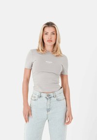 Grijze aansluitende t-shirt met korte mouwen en een ronde hals, met "SIXTH JUNE PARIS" in het wit over de borst gedrukt. Lichtblauwe hoge taille jeans.