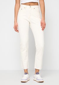 Jeans blancos ajustados con un diseño de pierna recta, fabricados en denim. Cuenta con un cierre de botón y cremallera, y un ligero deshilachado en los tobillos.