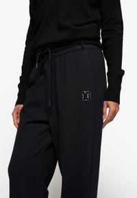 Czarne dresy wykonane z miękkiego materiału, posiadające elastyczny pasek na talii, sznurki do regulacji oraz haftowaną białą cyfrę "10" na lewej udzie.