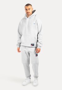 Felpa grigia con cappuccio e tasca frontale, decorata con un logo blu. Abbinata a pantaloni della tuta grigi coordinati, con toppe logotipo e una vestibilità comoda.