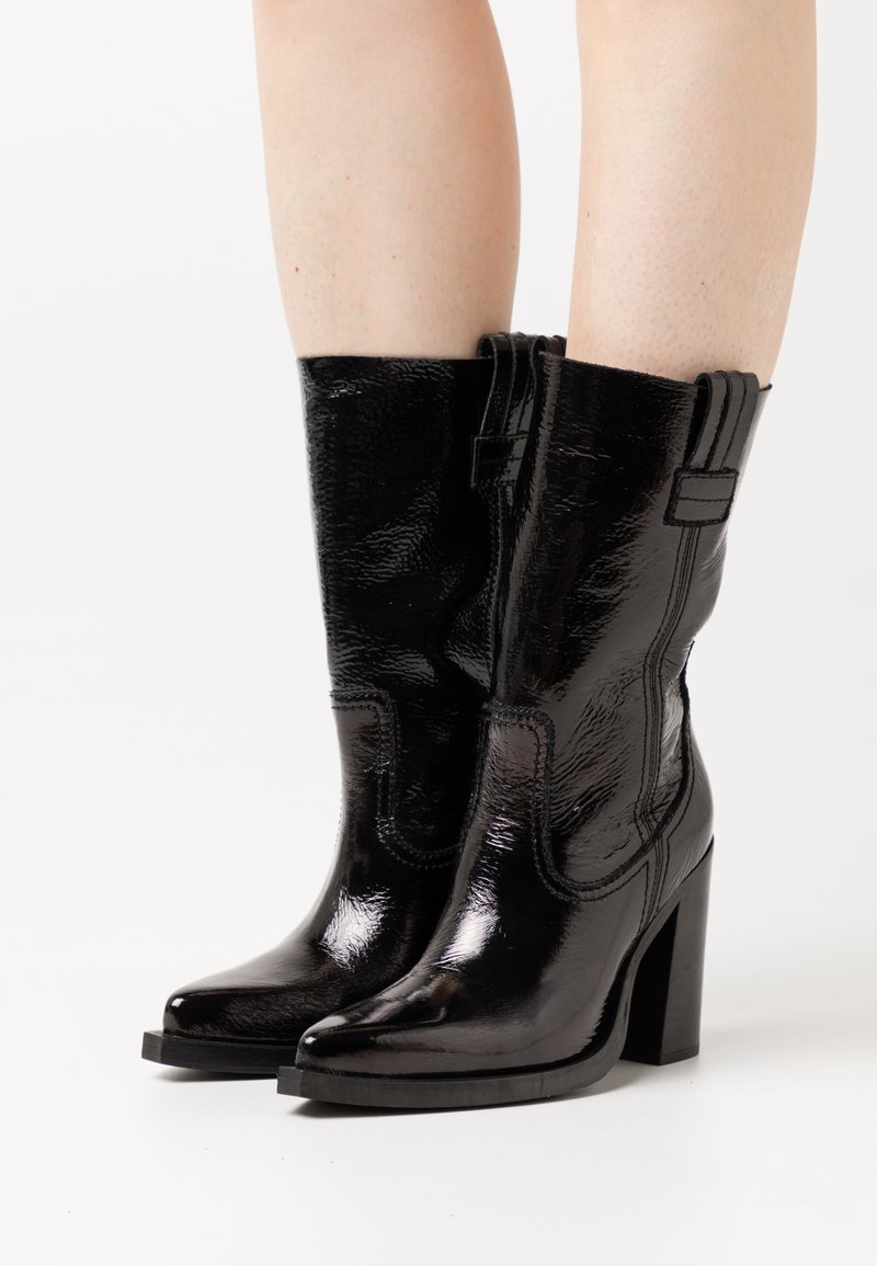 Black patent leather ankle boots with a pointed toe, chunky heel, stitch detailing, and contrasting black accents at the top.