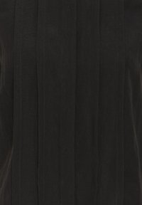 Musta pystysuora laskostettu kangas, jossa on hienovarainen rakenne ja ompeludetaljit, todennäköisesti osa vaatetusta.