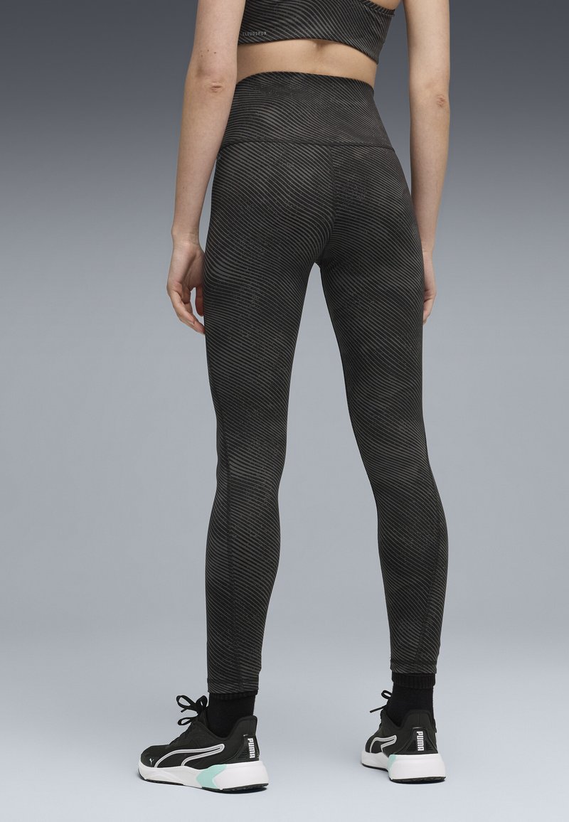Hoge taille legging in zwart met een geribbelde textuur en subtiele lijnpatronen, gedragen met zwarte sportschoenen met een mintaccent.