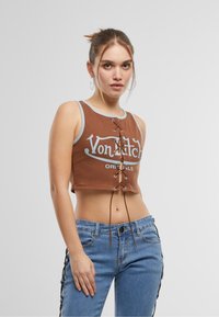 Brun crop topp med lyseblå kant og frontlisse, sammen med blå jeans med sideakenter. Bomullsmateriale, uformell design.