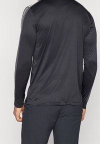 Maglietta sportiva a maniche lunghe nera, caratterizzata da una texture liscia, un fit slim e strisce laterali grigie a contrasto lungo le maniche.