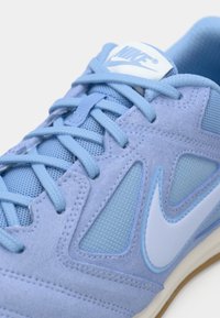 Ανοιχτό μπλε αθλητικό παπούτσι Nike με πλέγμα και σουέτ πάνελ, μπλε κορδόνια, λευκή σόλα και λευκό λογότυπο Nike στο πλάι και στη γλώσσα.