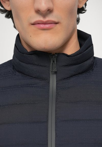 Temno mornarska jakna z visokim ovratnikom, z zadrgo in teksturiranim materialom z vzorcem logotipa Emporio Armani v tonirani zasnovi.