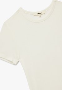 Camiseta de manga corta y cuello redondo en suave algodón color blanco roto, con una textura lisa y una etiqueta con el nombre de la marca en el interior del escote.