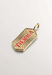 Colgante dorado con letras rojas en relieve que dicen "TIERRA" y líneas texturizadas radiantes sobre un fondo claro.