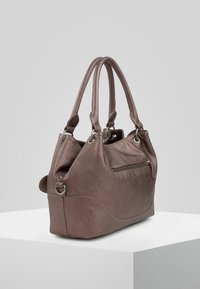 Brązowa skórzana torebka na ramię z podwójnymi uchwytami u góry, zewnętrzną kieszenią na zamek błyskawiczny oraz srebrnymi akcentami, umieszczona na białym podwyższeniu na szarym tle.