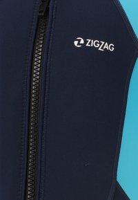 Une combinaison de plongée bleu marine avec des accents turquoise. Elle dispose d'une fermeture éclair noire et du logo "ZIGZAG" en blanc. Fabriquée en matériau flexible et résistant à l'eau.