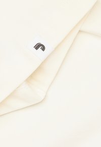 Off-white katoenen stof, gladde textuur, gevouwen en toont het label met een logo in donkergrijs. Minimalistisch ontwerp met scherpe randen.