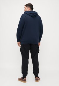 Navy blue hooded sweatshirt with ribbed cuffs, paired with black cargo pants featuring side pockets, and brown sneakers.