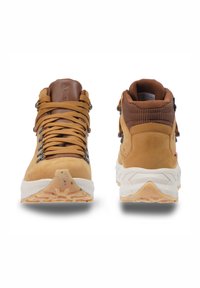 Tan hiking boots featuring a suede upper, padded brown collar, metal hardware, and textured rubber outsole with multicolored speckles.