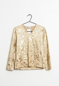 Gul metallisk långärmad skjorta med V-ringning, prydd med ett sprutmönster och slät, glansig yta. Visas på en galge.