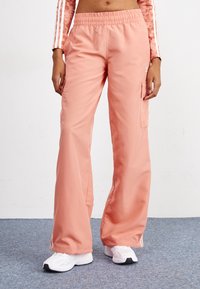 Vaaleanpunaiset cargo-housut, joissa on joustava vyötärö, leveät lahkeet ja sivutaskut. Materiaali näyttää sileältä ja kevyeltä, sopii arkipukeutumiseen.