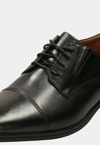 Zapato de vestir negro de cuero con cierre de cordones, punta afilada, detalles de costura sutiles y un acabado suave. Adecuado para ocasiones formales.