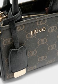 Close-up van een zwarte handtas met een monogram patroon en een gouden "LIUJO" logo, met korte handvatten en een ritssluiting.