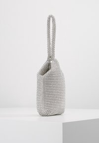 Sac à main en sequins argentés avec une texture perlée, une forme arrondie, et une seule poignée, doté d'une fermeture éclair et d'un intérieur lisse.