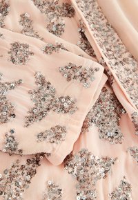 Blush fabric featuring intricate silver sequin embellishments in floral patterns, with soft texture and layered folds visible.