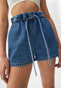 Shorts de mezclilla con cintura elástica y cordón, con un lavado azul, un ligero deshilachado en el dobladillo y bolsillos laterales.