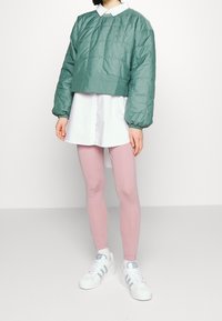 Virkat puffer-jacka i grönt, vit kavaj under, rosa leggings och vita sneakers med blå accenter. Standard passform.