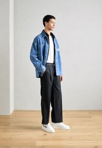 Vaate denim-takki vaaleansinisenä, jossa on rintatasku, päällä musta paita ja valkoinen T-paita, yhdistettynä mustiin leveälahkeisiin housuihin ja valkoisiin tennareihin.