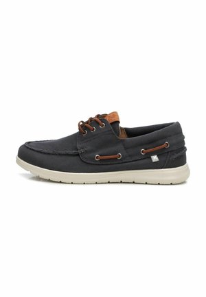 Zapatilla de barco de lona gris oscuro con cordones marrones y un acento beige en el talón, que presenta una suela de goma blanca y costuras en contraste.