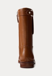 Brune lærstøvletter til knæet med en glat tekstur, afrundet tå og træhæl. Har en side-rem med metalhardware.