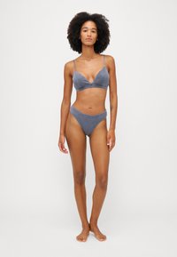 Szary bikini w dwóch częściach wykonane z miękkiego materiału. Biustonosz ma cienkie ramiączka i dekolt w kształcie litery V, podczas gdy dół bikini ma wycięcie w stylu high-cut.