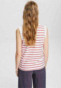 Top blanco sin mangas con rayas rojas horizontales, material de algodón suave, escote redondo y dobladillo curvado, combinado con pantalones holgados color marino.