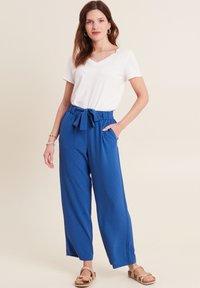 Pantaloni larghi a righe blu con cintura annodata, abbinati a una t-shirt bianca a scollo a V e sandali strappy color marrone chiaro.