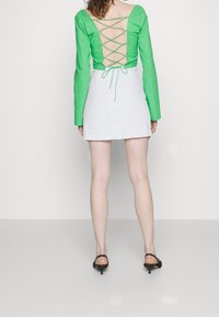 Vihreä pitkähihaisuus paita, jossa on pitsiyksityiskohtainen selkä, yhdistetty valkoiseen minihameeseen. Asu on vartalonmyötäinen ja siinä on minimaalinen määrä metalliosia.