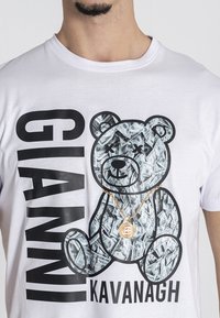 Camiseta de algodón blanca con un gráfico de un oso lleno de billetes de dólar, con el texto "GIANNI KAVANAGH" en letras negras en negrita.