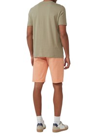 Oliwkowa koszulka z krótkim rękawem połączona z jasnoróżowymi szortami. Model nosi białe skarpetki i beżowe sneakersy z granatowymi akcentami.