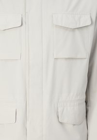 Light gray jacket with four front pockets, a zip closure, and a smooth, textured fabric. Features a straight cut and subtle stitching details.