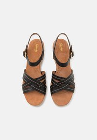 Sorte svarte lær sandaler med kryssdesign, ankelrem og polstret tan fotseng, med en lysfarget såle og sømdetaljer.