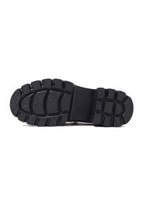 Suola di scarpa in gomma nera con scanalature profonde, dotata di una sezione centrale rialzata e motivi vari per una migliore aderenza. Design resistente e robusto.