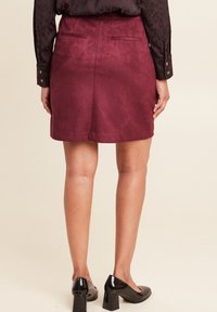 Bordeaux suede minirok met twee achterzakken, rechte zoom, gecombineerd met zwarte lakleren blokhakken.