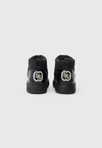 Sorte ankelstøvler lavet af polstret materiale med en tekstureret gummisål. Har et metallisk logo på hælen med rhinestones.