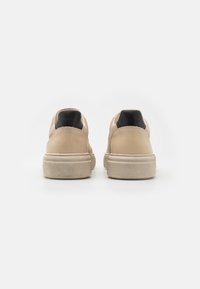 Béžové tenisky na platformě s černými patními pásky, zobrazené zezadu na bílém pozadí.