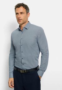 Blau gemustertes Langarmhemd mit Button-Down-Kragen, tailliertem Schnitt und kontrastierenden Knöpfen. Kombiniert mit dunkler Hose und schwarzem Gürtel.