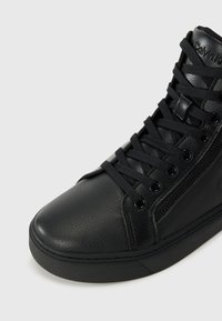 Black high-top sneaker crafted from textured leather, featuring flat laces, a side zipper, and a thick rubber sole.