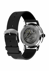 Zegarek Timex z stalową obudową, przezroczystym tyłem i czarnym gumowym paskiem. Posiada widoczny mechanizm oraz okrągły, minimalistyczny design.