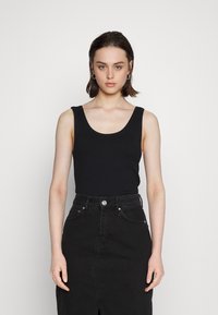 Top preto de alças largas, com decote arredondado, combinado com uma saia de ganga preta de cintura alta, com uma abertura frontal e detalhe de botão prateado.